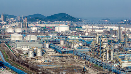Obraz premium Aerial view of petrochemical industrial zone with large storage tanks and port terminals by the sea.