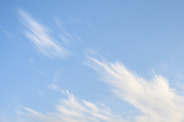 Late afternoon sunny blue sky with light diagonal flow of white wispy clouds, as a nature background
