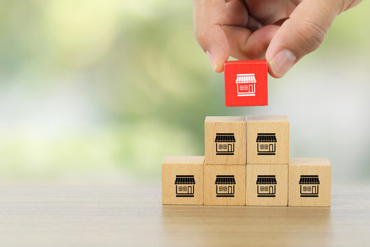 Hand chooses wooden toy block stack with franchise business store for target goal and franchising to growth branch expansion and business banking loan or consumer resources service.
