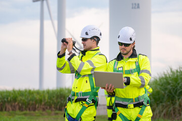 Wind farm technicians inspecting turbines with tools and equipment in green field