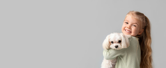 Cute little girl hugging Maltese dog on grey background