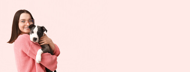 Beautiful young woman in eyeglasses with cute staffordshire terrier puppy on pink background