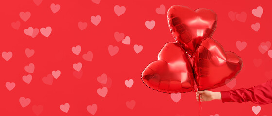 Fototapeta premium Female hand with air balloons in shape of heart on red background. Valentine's Day celebration