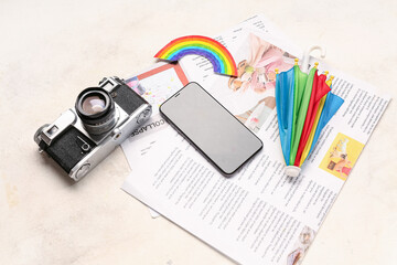 Fototapeta premium Mobile phone with photo camera, rainbow, umbrella and newspapers on grunge background. Weather forecast concept
