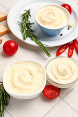 Bowls of tasty cream cheese on white tile background