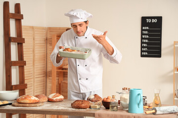 Handsome young chef holding baking dish with fresh croissants in bakery