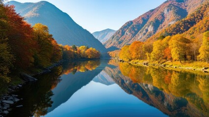 Obraz premium Golden autumn foliage reflects in a tranquil mountain river under a clear blue sky, showcasing the vibrant beauty of the changing season and serene natural landscape