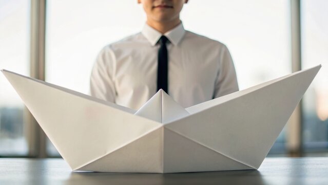 A man in a shirt and tie presents a large paper boat, symbolizing creativity and innovation in a bright, modern setting.