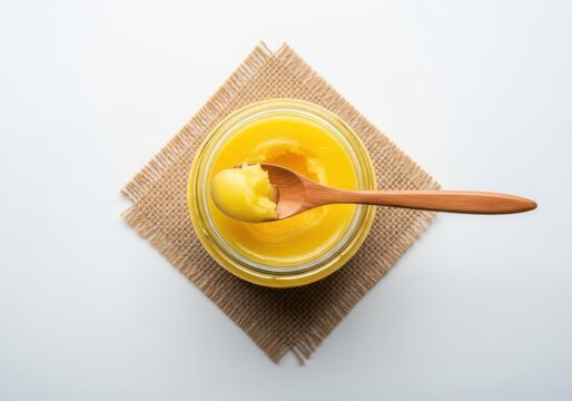 Golden ghee in jar with wooden spoon, top view, white background