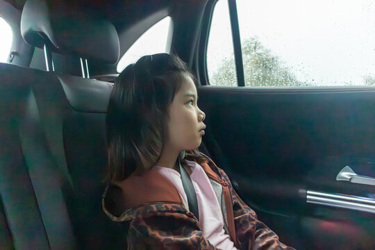 Asian girl looking out the car window at the rain and raindrops, captured in a moody atmosphere during a rainy day journey
