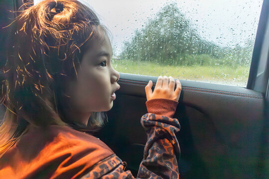 Asian girl looking out the car window at the rain and raindrops, captured in a moody atmosphere during a rainy day journey - Powered by Adobe