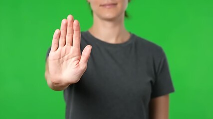Woman emphatically gesturing stop on vibrant green screen for safety awareness or social issue campaign, perfect for impactful messaging and presentations