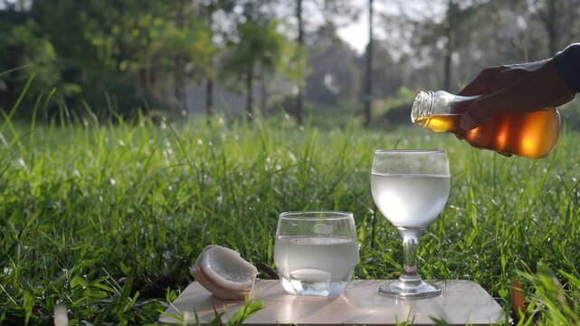 Coconut perfume water mixed with wild honey in a glass on a wooden floor in the grass.