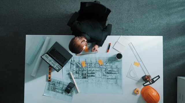 Time lapse of smart architect drawing while working at laptop. Top down view of caucasian engineer designing blueprint and drafting house model at table with equipment and safety helmet. Alimentation.