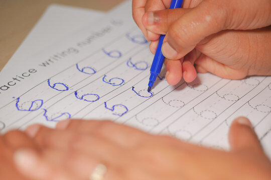 Child practicing writing numbers at a desk in a classroom