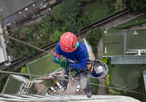 a worker wearing a safety helmet and a harness, suspended by ropes access on the exterior of a high-rise building.