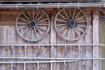 古民家の壁に目玉のように吊り下げられた木製の農機具の車輪とはしご