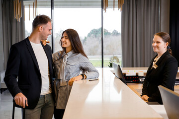 Couple and receptionist at counter in hotel. Young couple on a business trip doing check-in at the hotel