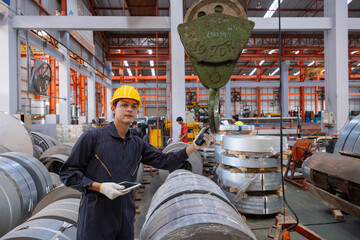 Factory worker operating crane hook for metal coils