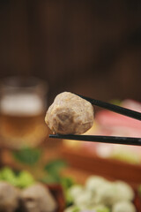 Hot Spicy Meatball in Chopsticks with Delicious Asian Food Ingredients Variety in Background