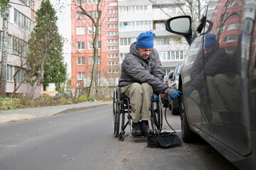 Obraz premium A man in a wheelchair connects a car compressor to a car wheel