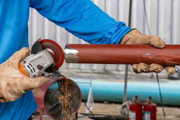 Worker using angle grinder on metal pipe