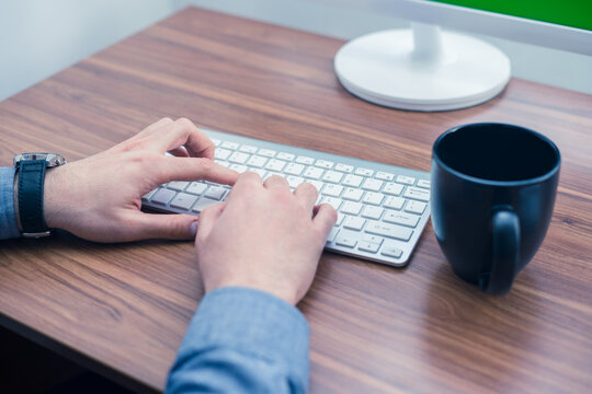 Hands typing on wireless keyboard on wooden table