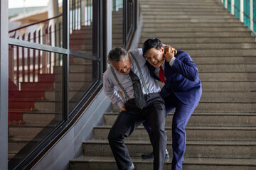 A young businessman in a suit supports and helps a senior colleague stand, reflecting intergenerational teamwork, empathy, and collaboration in a modern, innovative business environment
