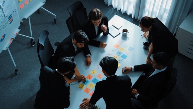 Top view of business people brainstorm idea by using sticky notes while planning marketing strategy at meeting room. Group of diverse team discuss about financial plan. Teamwork concept. Directorate.