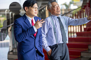 Two businessmen of different generations in formal suits networking and discussing ideas outside an office, representing workplace mentorship, collaboration, and professional growth.