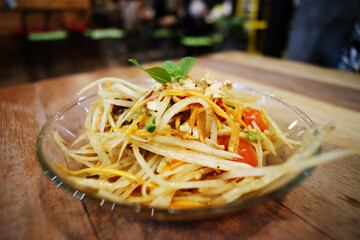 Spicy papaya salad in glass bowl on wooden table
