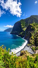 Dramatic coastal scene with dark beach, turquoise water, and lush green cliffs/mountains