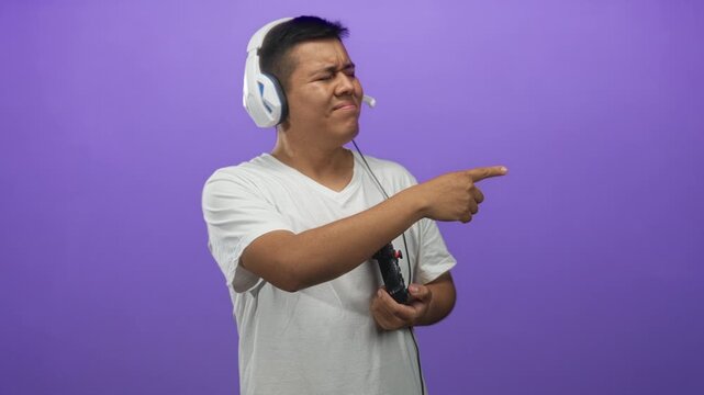 Man pointing finger while holding game controller and wearing headset in purple studio; concentration gaming.