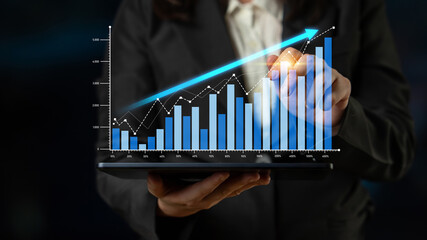 A business professional evaluates digital financial data on a tablet, displaying a growth chart. The scene emphasizes technology and success in the corporate setting. Scalp