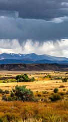 Dramatic landscape with prairie grasses, distant mountains, and a stormy sky above