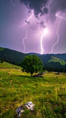 Dramatic lightning strikes behind a tree-filled, grassy meadow and wooded hills
