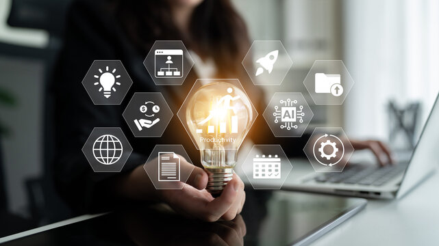 A business professional holds a light bulb symbolizing innovation, surrounded by technology icons representing productivity and engagement in a modern office space. Gantry - Powered by Adobe