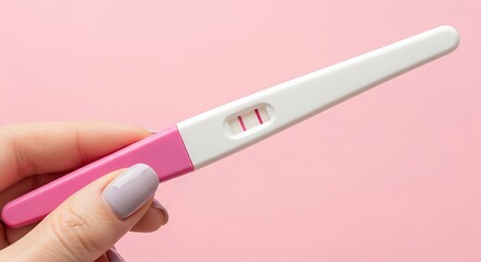 Closeup of a hand holding a positive home pregnancy test stick against a soft pink background, showing two lines Background image