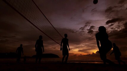 Young people playing beach volleyball by the ocean at sunset