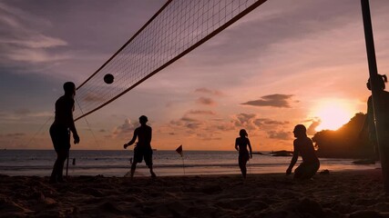 Young people playing beach volleyball by the ocean at sunset