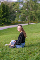Girl enjoying the summer breeze with phone, sitting on a grassy hill near the University buildings