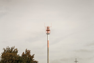 Lone communication tower stretches toward overcast sky, bordering field of green trees near rural area