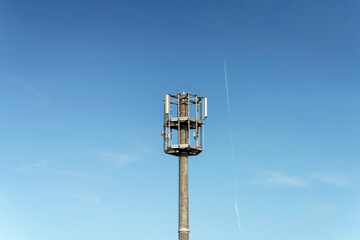 Communication antenna rises above the clear blue, contrail piercing the sky