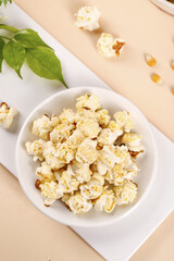 Fresh Popcorn in White Bowl with Green Leaves on Beige Background