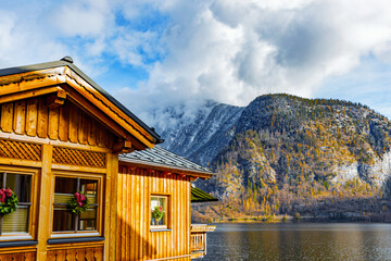 A traditional charming wooden Hallstatt lakeside home in front of dreamy view of the lake and mountains. The scenic background features a steep, snow-dusted Alpine mountain.
