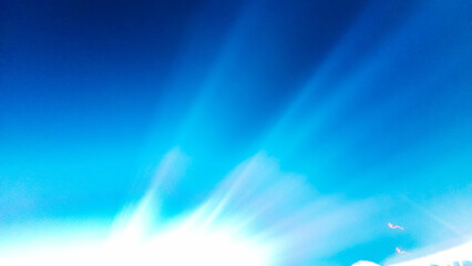 Dramatic white light rays radiate upward from a point source in the center, against a bright and deep electric blue background
