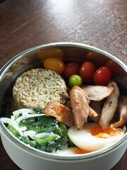 healthy lunch box with steamed young jasmine brown rice, grilled chicken, boiled egg, spinach and onion salad and fresh cherry tomatoes