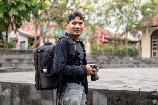 Indonesian photographer walking with camera and backpack outdoors