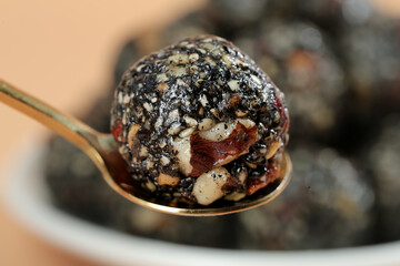 Healthy energy ball with black sesame seeds and nuts on copper spoon closeup