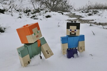 Naklejka premium LEGO Minecraft figures of Steve and Alex trudging in deep snow on edge of winter agricultura field during cloudy winter day. 